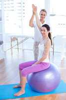 Trainer helping woman on exercise ball