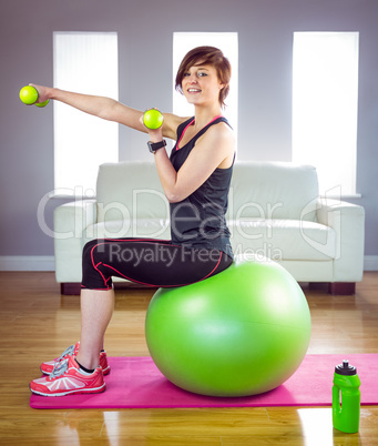 Fit woman lifting dumbbell sitting on ball