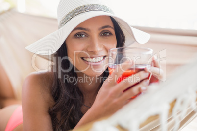 Pretty brunette relaxing on a hammock and drinking cocktail