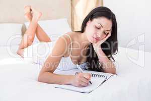 Pretty brunette writing and thinking on bed