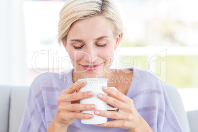 Pretty blonde woman relaxing on the couch and holding a mug