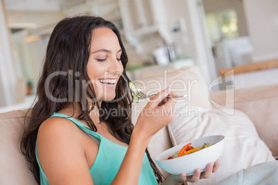 Pretty brunette eating salad on couch