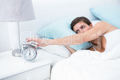 Pretty brunette extending hand to alarm clock