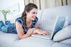 Happy woman lying on couch using her laptop