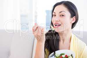 Pretty brunette looking at camera and eating vegetables