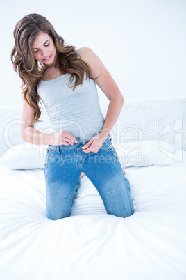 Attractive woman putting on tight jeans on a bed
