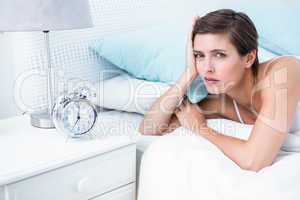 Beautiful young woman lying in bed with alarm clock