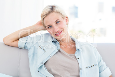 Pretty blonde woman sitting on the couch and smiling at the came Pretty blonde woman sitting on the couch and smiling at the came