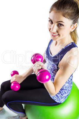 Fit woman lifting dumbbell sitting on ball