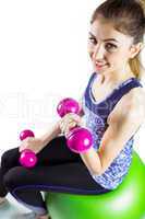 Fit woman lifting dumbbell sitting on ball