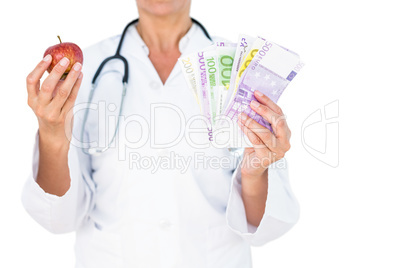 Confident female doctor holding red apple and banknotes