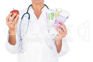 Confident female doctor holding red apple and banknotes