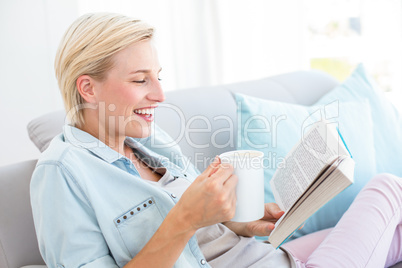 Pretty blonde woman reading a book and holding a mug