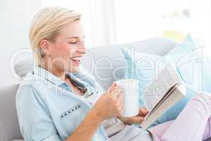 Pretty blonde woman reading a book and holding a mug