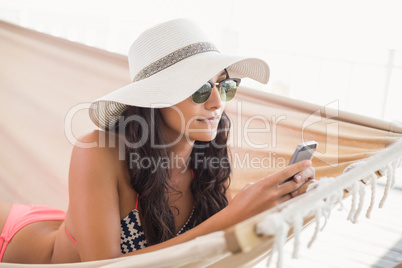 Pretty brunette relaxing on a hammock and texting with her mobil