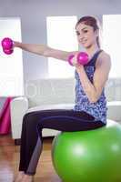 Fit woman lifting dumbbells on exercise ball