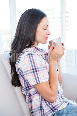 Pretty brunette holding hot beverage on couch