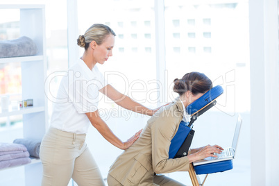 Businesswoman having back massage while using her laptop