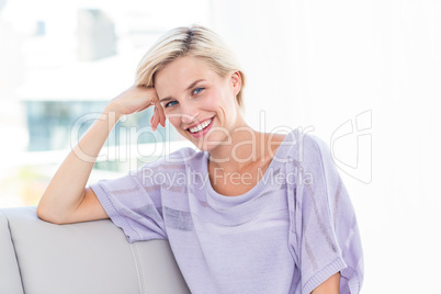 Pretty blonde woman sitting on the couch and smiling at the came