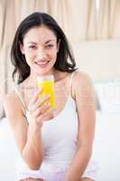 Pretty brunette holding a glass of orange juice on bed