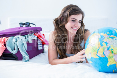 Woman with a suitcase and globe while lying on her bed