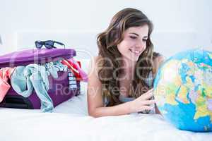 Woman with a suitcase and globe while lying on her bed