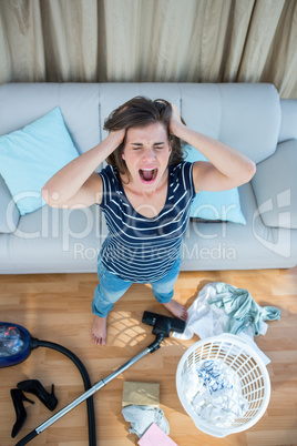 Angry woman in a chaotic living room with vacuum cleaner