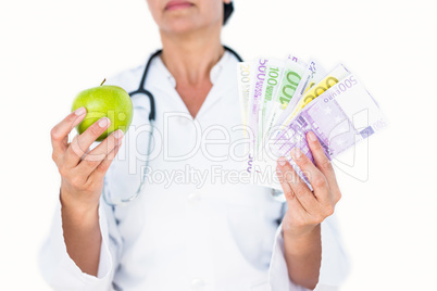 Confident female doctor holding green apple and banknotes
