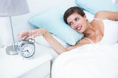 Happy woman extending hand to alarm clock