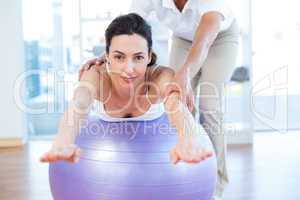 Trainer helping woman on exercise ball