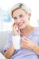 Pretty blonde woman sitting on the couch and holding a mug