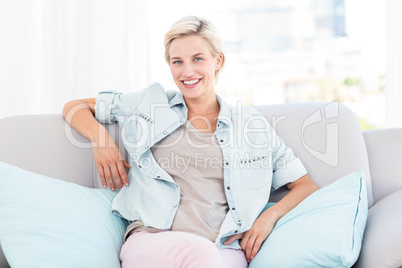 Pretty blonde woman sitting on the couch and smiling at the came