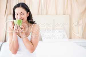 Pretty brunette drinking hot beverages on bed