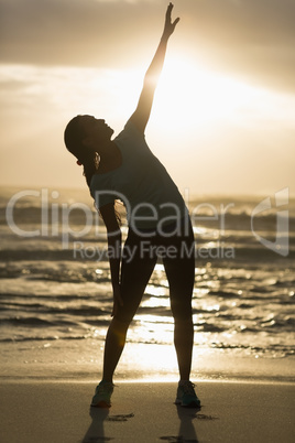 Sporty brunette stretching on the beach