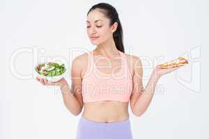 Smiling brunette looking at salad while holding pizza