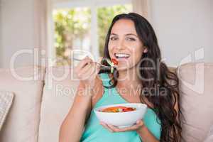 Pretty brunette eating salad on couch