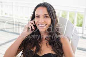 Pretty brunette sitting on a chair and calling with her mobile p