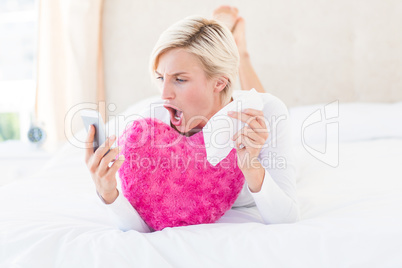 Shocked blonde woman lying on the bed and texting with her mobil