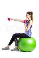 Fit woman lifting dumbbell sitting on ball