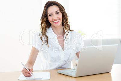 Smiling businesswoman working with her laptop and taking notes