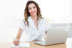 Smiling businesswoman working with her laptop and taking notes