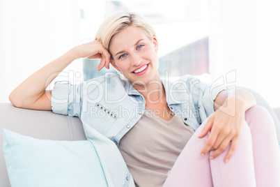 Pretty blonde woman sitting on the couch and smiling at the came