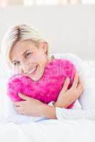 Smiling blonde woman holding heart pillow