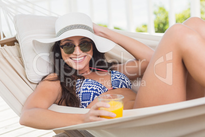 Pretty brunette relaxing on a hammock and drinking orange juice