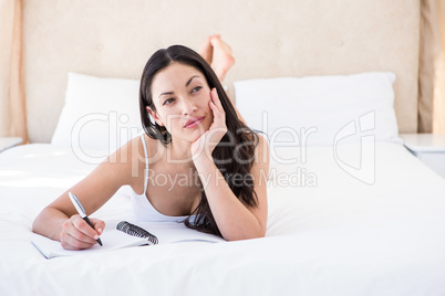 Pretty brunette writing and thinking on bed