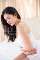 Pretty brunette with stomach pain on bed