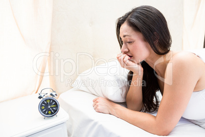 Pretty brunette watching alarm clock on bed