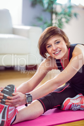 Fit woman looking at camera and stretching on exercise mat