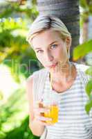 Pretty blonde woman smiling at the camera and drinking orange ju