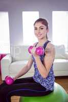 Fit woman lifting dumbbells on exercise ball